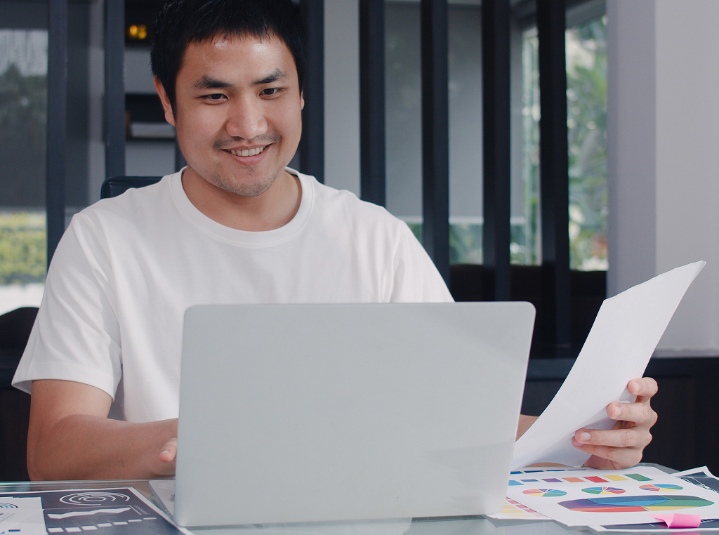 Young Asian businessman recording income and expenses on a laptop — offshore accounting role